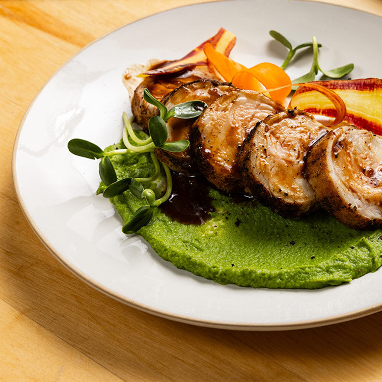Roasted rabbit loin with pea puree and carrot ribbon salad on a white plate. 
